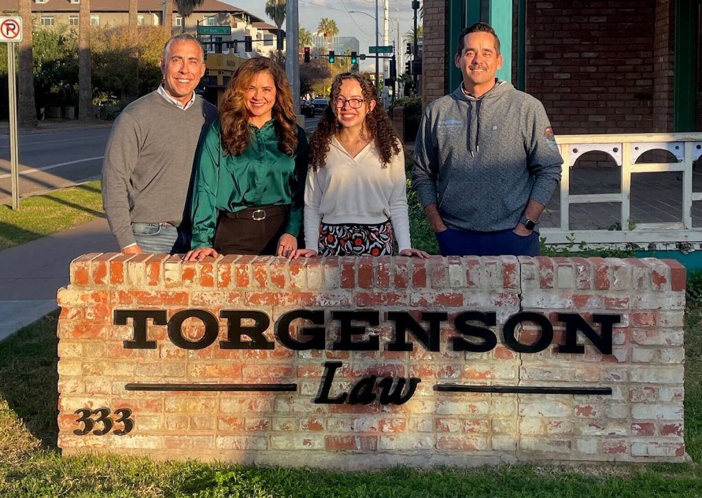 Four people stand behind a brick wall with the TORGENSON Law 333 sign, as featured in the winter newsletter.