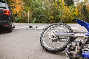 A motorcycle lies on its side near a car at a crosswalk, with scattered debris around