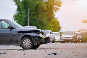 Damaged black car with a crumpled front bumper on a busy road