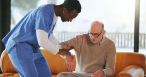 woman in blue scrubs helping an elderly man in a waiting room