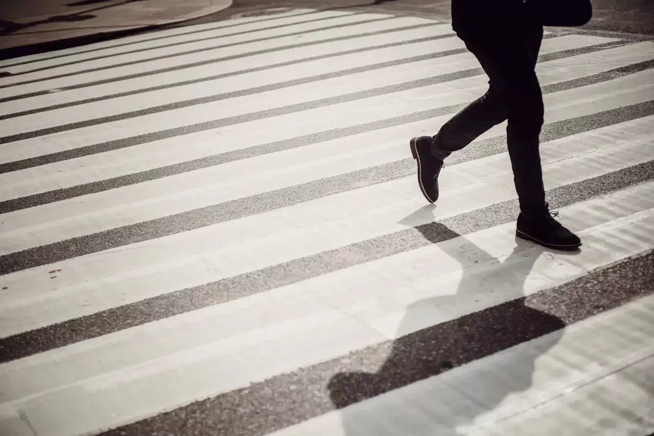 A person walking across a striped pedestrian crosswalk.