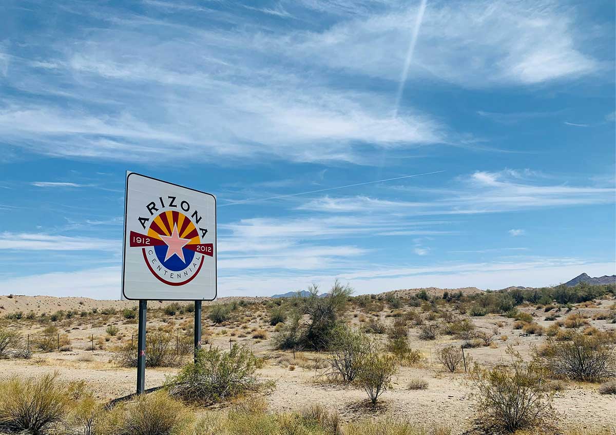 A sign featuring the Arizona Centennial emblem standing in a desert landscape under a blue sky.