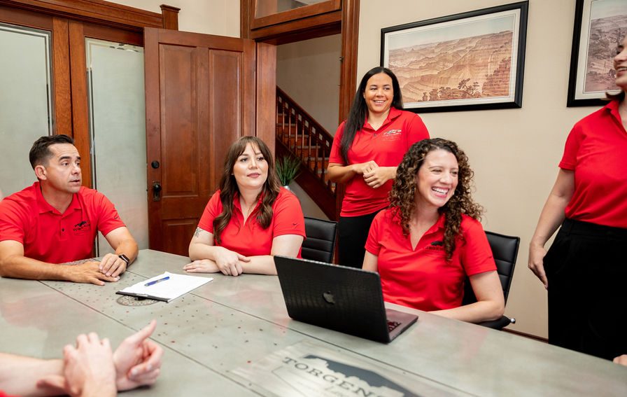 Five people in red polo shirts sit or stand around a conference table during a meeting.