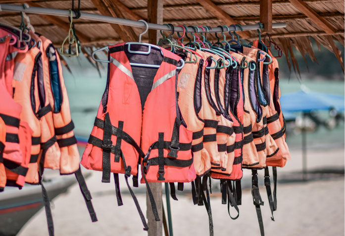 A row of orange life jackets, essential for preventing personal injury, hanging on a rack under a thatched roof at the beach.