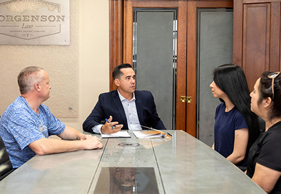 A lawyer in a suit sits at a conference table, speaking with three rideshare clients.