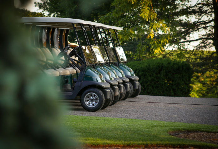A row of dark green golf carts parked in a line on a paved path, a common site for personal injury risks.