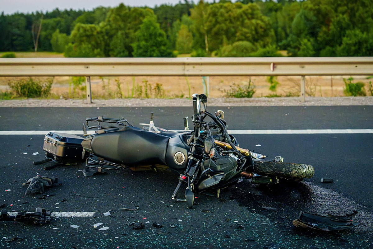 A motorcycle lies on its side on a road following an accident, with debris scattered around it.