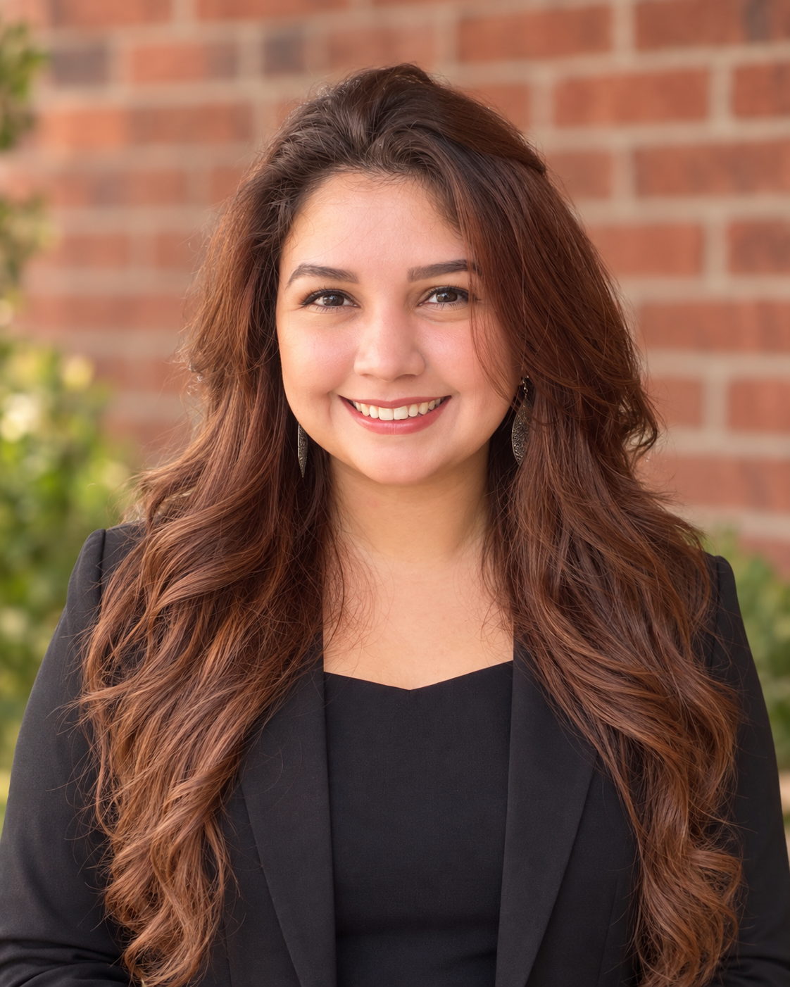 A professional headshot of Natalie Villarreal, a smiling woman with long brown hair wearing a black blazer.
