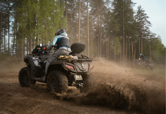 A person riding an ATV kicks up a cloud of dust while driving through a pine forest, a common setting for personal injury incidents.
