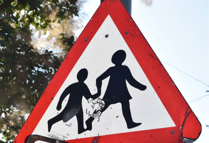 Triangular school crossing road sign showing silhouettes of two children holding hands, a common site near personal injury risk zones.