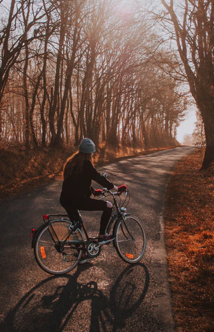 A person riding a bicycle down a tree-lined road during the autumn, mindful of their personal injury rights while cycling.