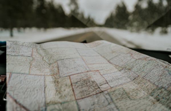 A paper map showing Wyoming and surrounding states resting on a car dashboard in front of a snowy, out-of-focus road.