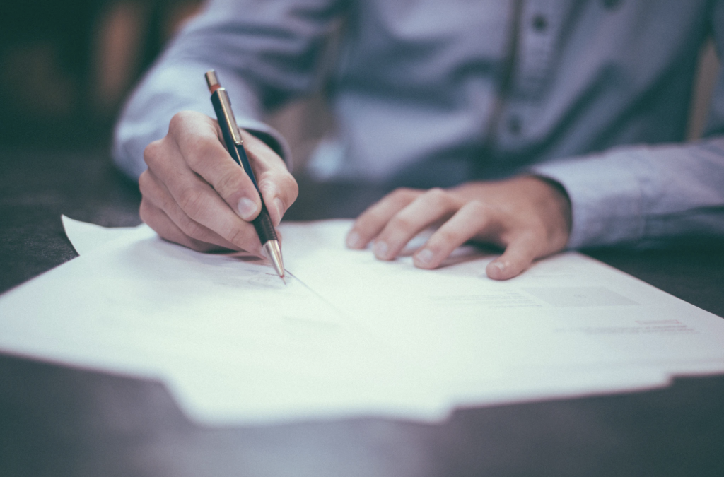 An expert witness in a button-down shirt writes on a piece of paper with a mechanical pencil.