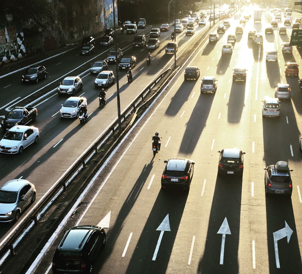 High-angle view of heavy traffic on a multi-lane highway at sunset, with vehicles changing lanes and casting long shadows across the road.