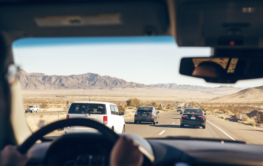 View from the drivers seat of a car traveling on a highway through a desert landscape with mountains in the distance.