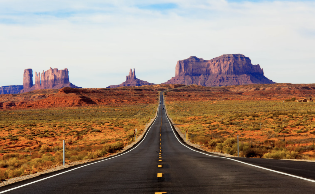 A long, straight highway stretches through a desert landscape toward red rock mesas in Monument Valley, a scenic route where motorists must remain alert to avoid car accidents.