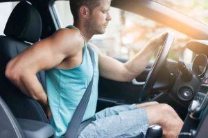 abogado de lesiones de espalda Un hombre sentado en un coche con la espalda dolorida