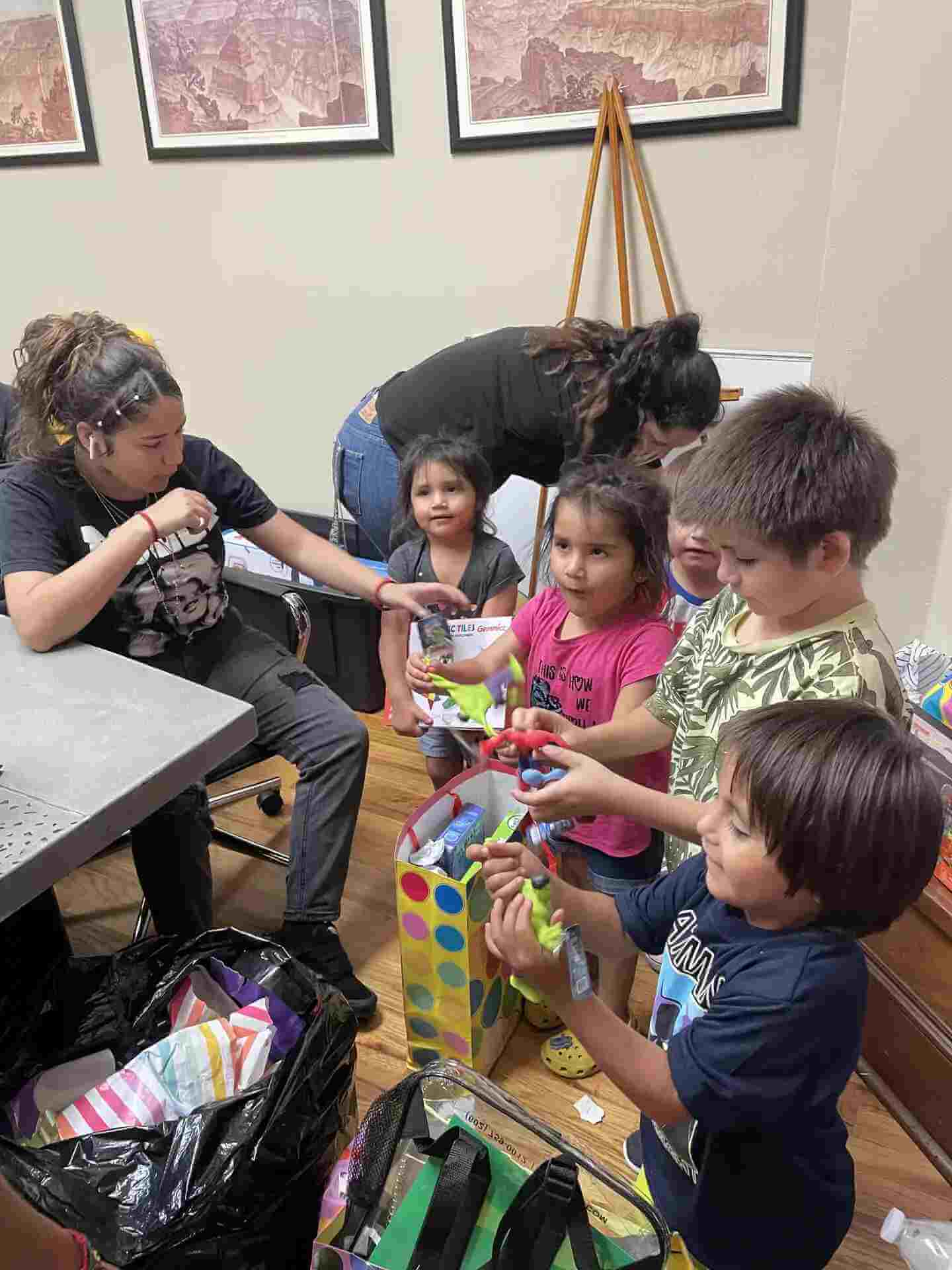 A woman hands small Christmas toys to a group of children gathered around a gift bag.