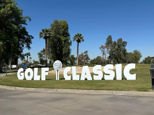 Large white letters spelling MAM’s 11th Annual Golf Classic on a grassy course, with a golf ball logo replacing the letter I.
