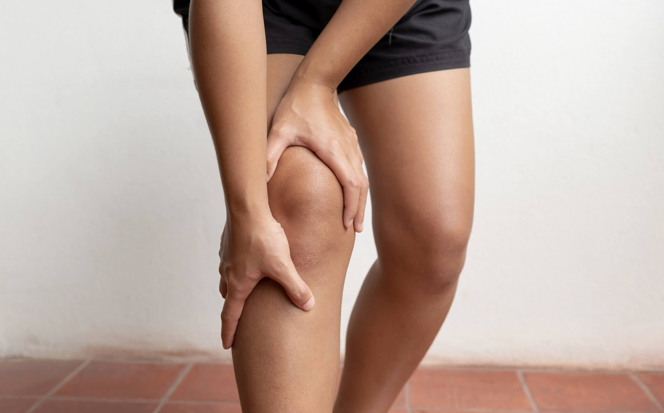 A person in athletic shorts clutching their knee in pain following a car accident.