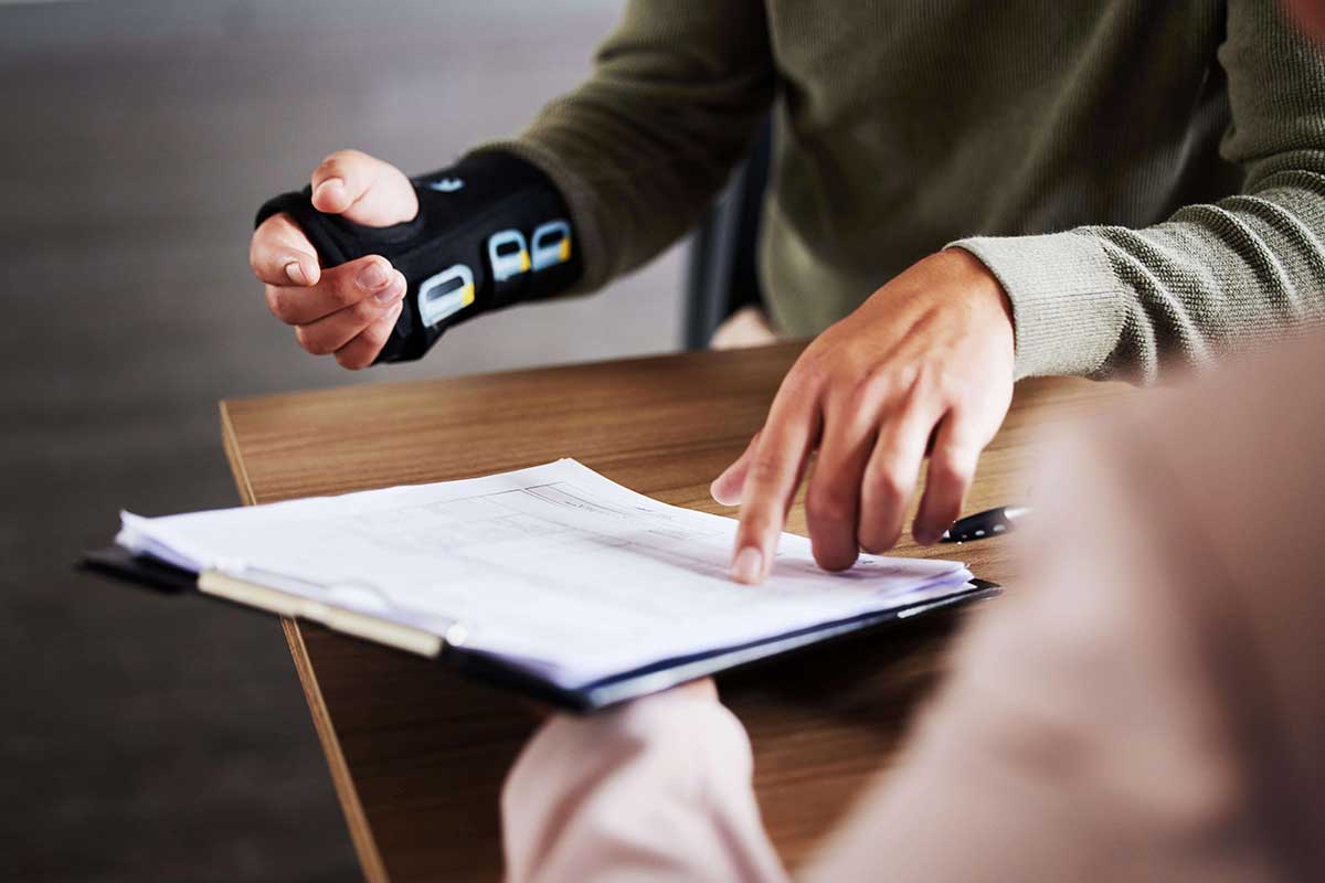 A person wearing a black wrist brace reviews a document on a clipboard with a distracted driver.