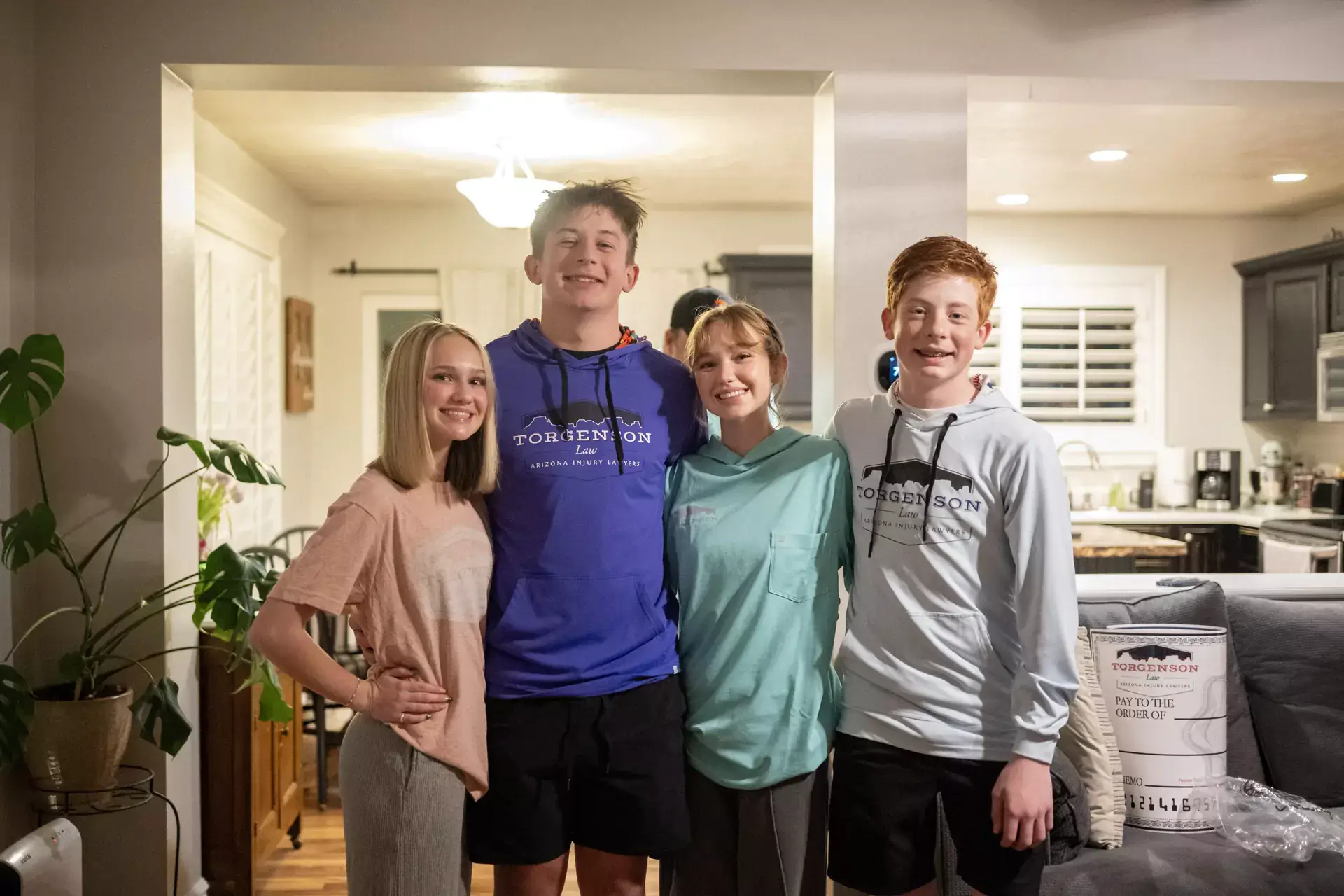 Four young people smile together in a living room, with two wearing Renee Torgenson Law hoodies.