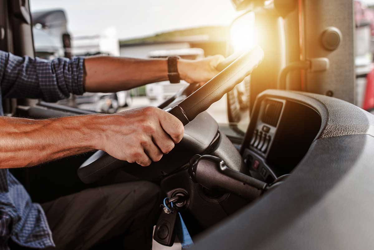 A persons hands gripping the steering wheel inside the cab of a truck.