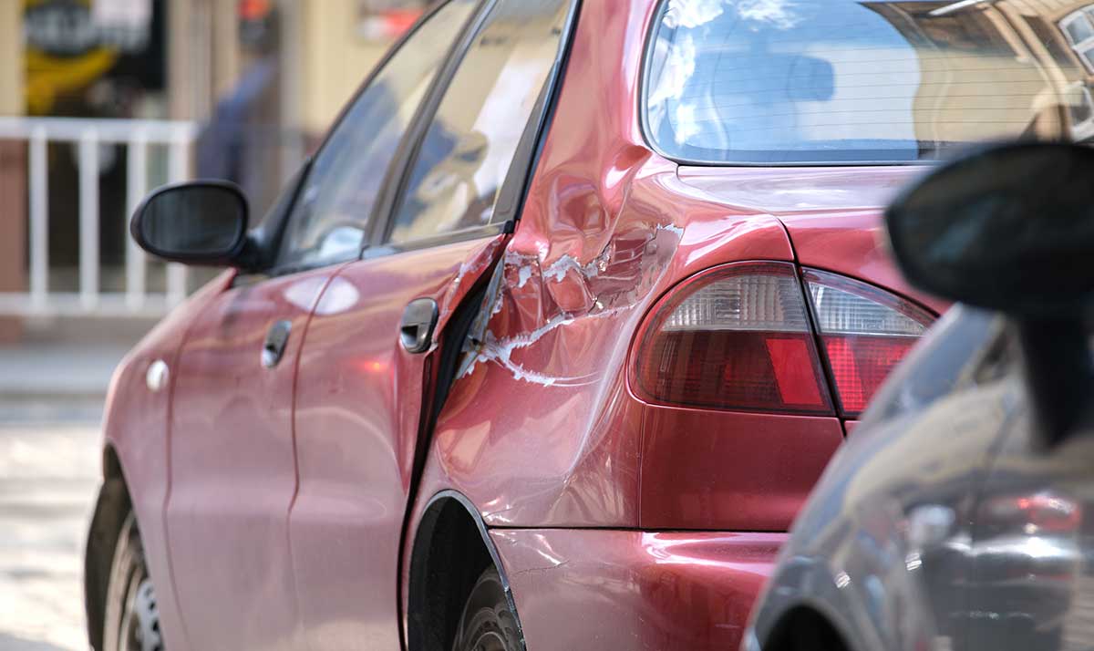 A red sedan with significant T-bone dent damage to the rear passenger-side door and quarter panel.
