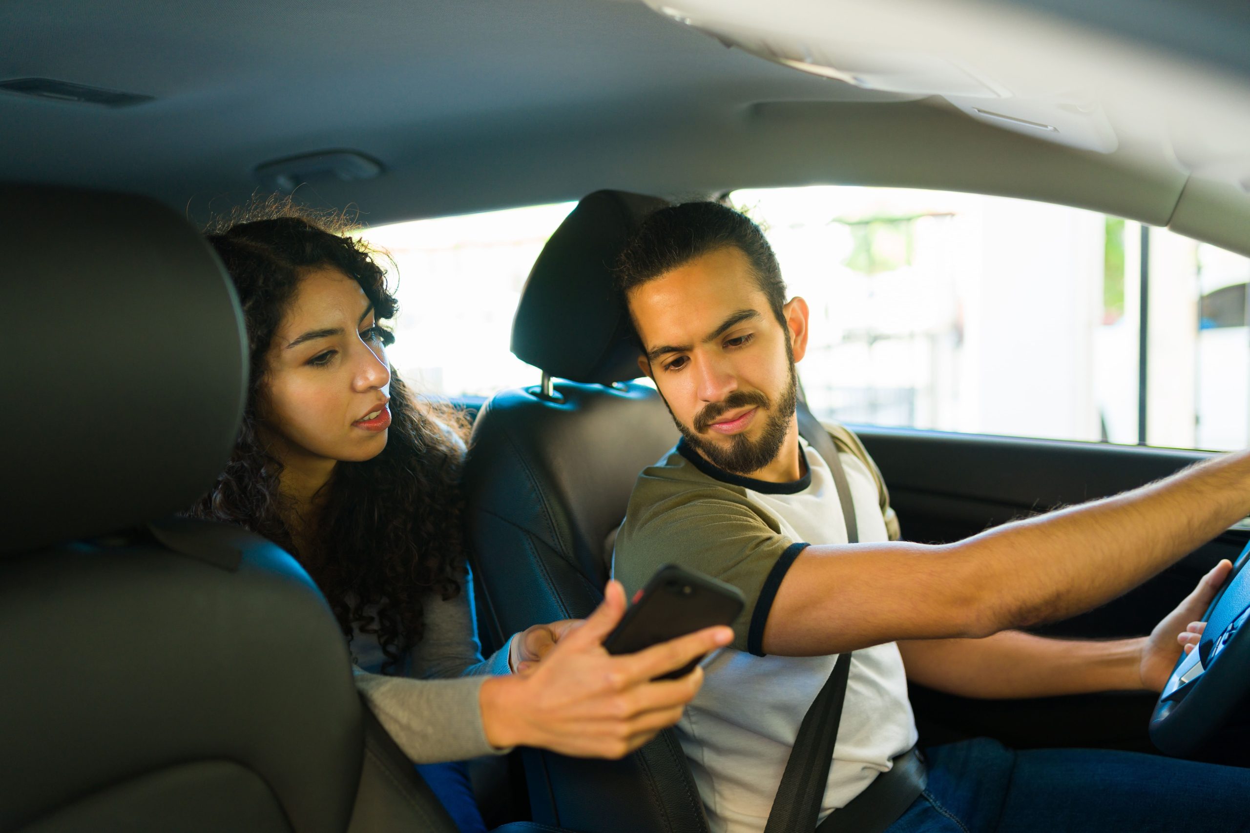 A woman in the back seat shows a phone to the driver