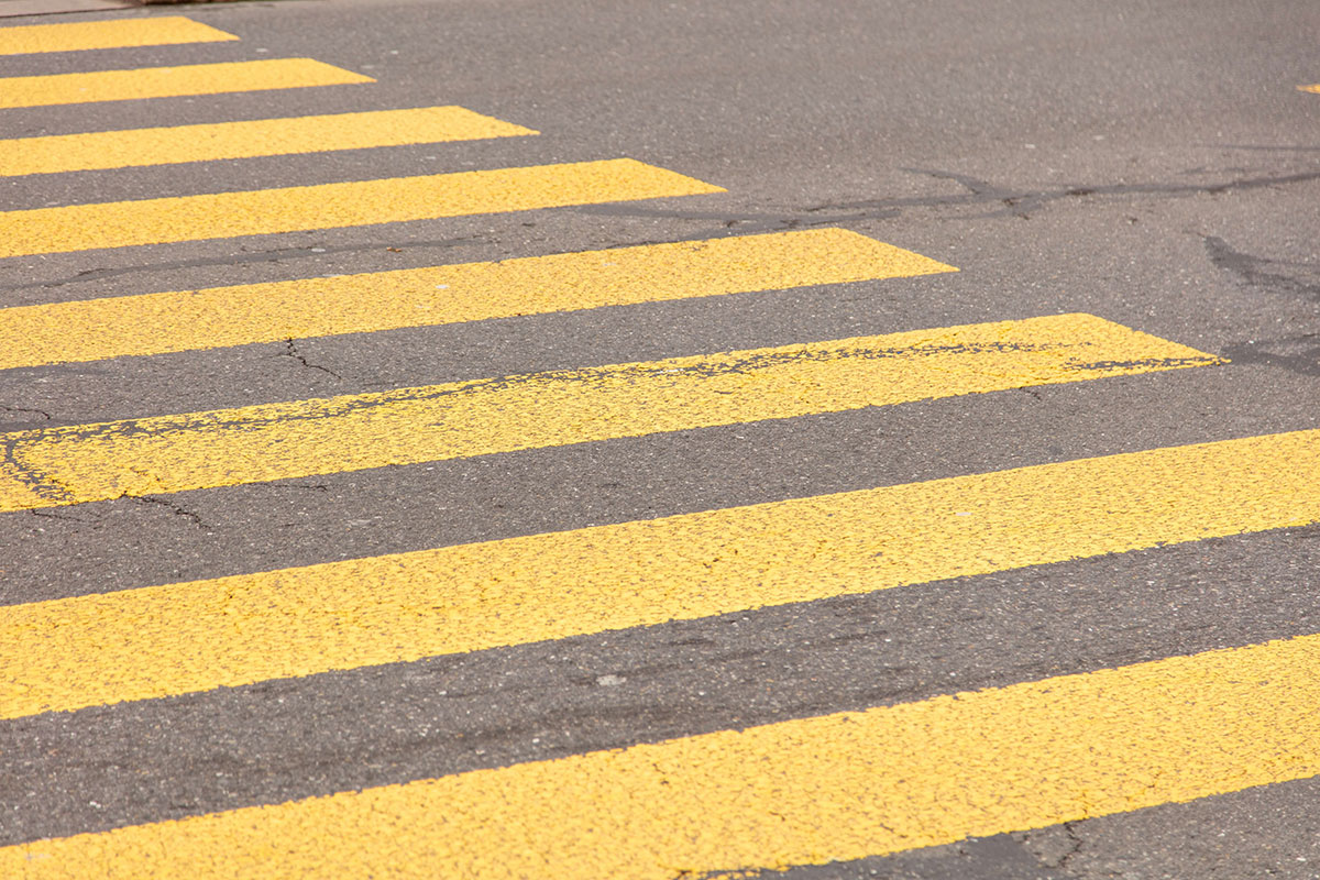 Yellow painted stripes of a pedestrian crosswalk on grey asphalt.