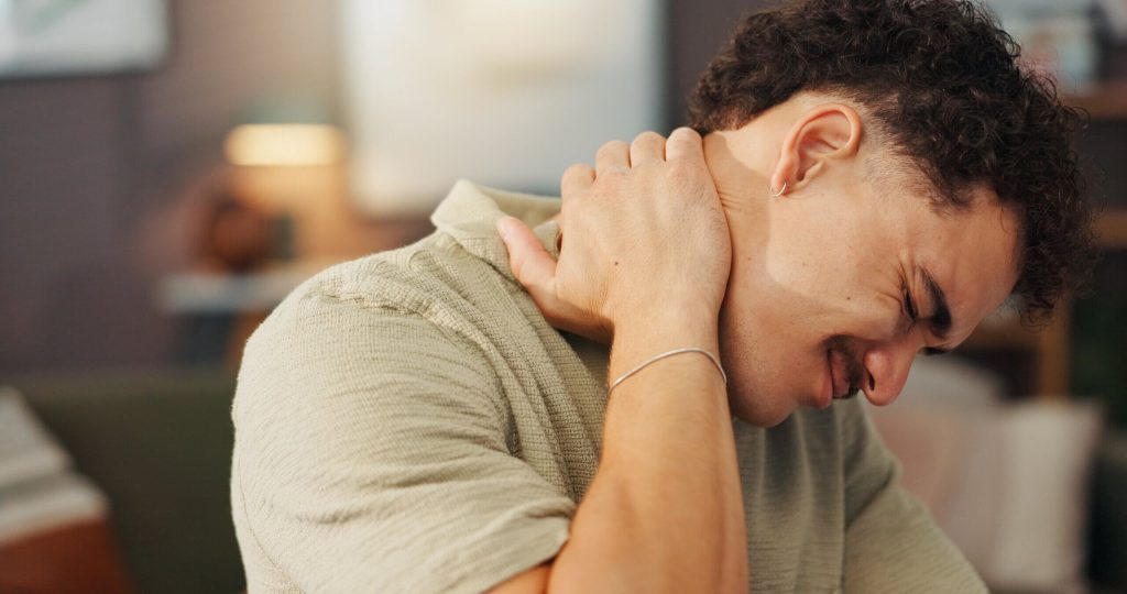 man grimacing and holding his neck in pain]