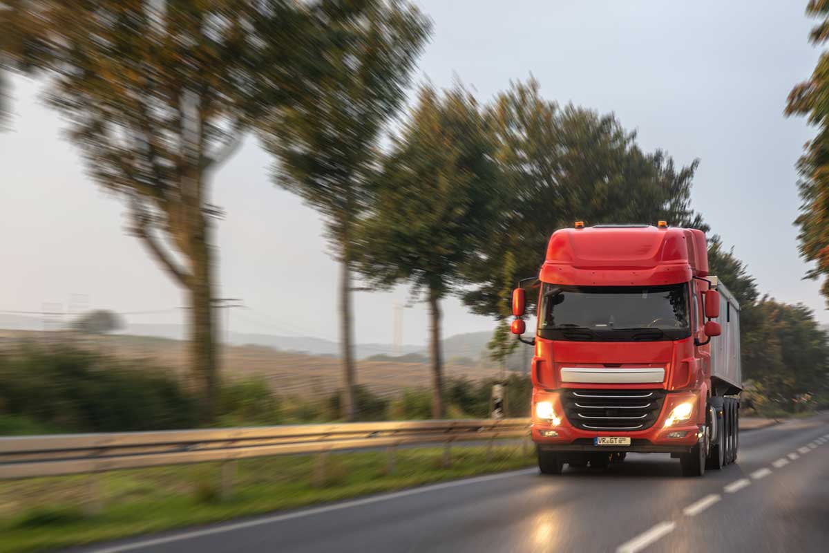 A red semi-truck involved in distracted driving moves along a tree-lined road.