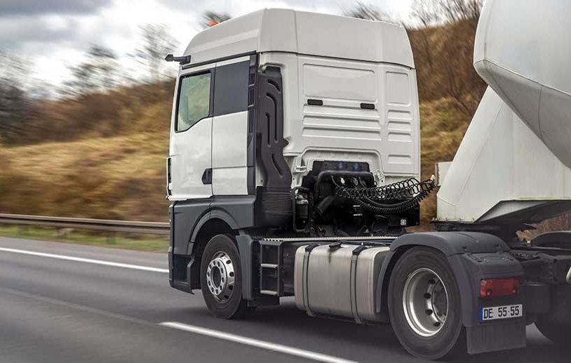A poorly maintained white semi-truck pulling a cement mixer drives along a highway.