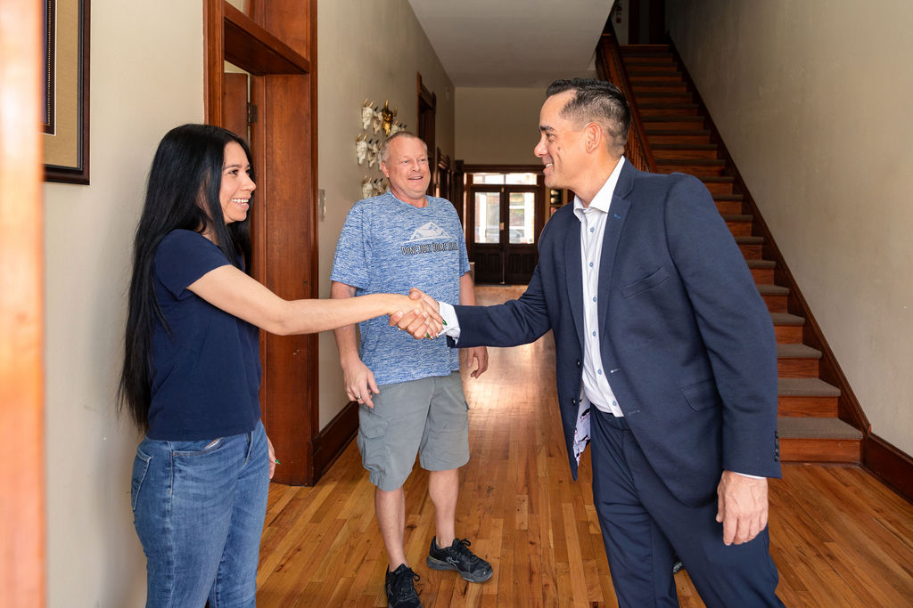 A woman and a man in a suit shake hands in a hallway, near a golf cart, while another man stands behind them.