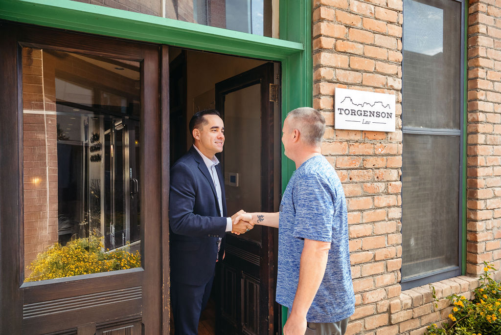 A man in a suit shakes hands with a man in a blue shirt at the entrance of Torgenson Law.