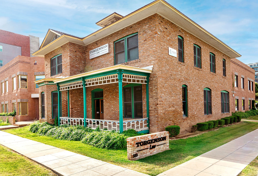 Two-story brick office building with a green-trimmed front porch and a Torgenson Law sign near the sidewalk, where the fatigue of the aged masonry shows.
