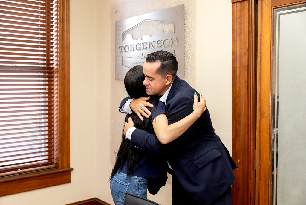 A man in a suit hugging a woman in front of a Torgenson Law office sign for our About Us page.