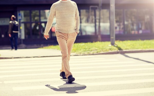 A person wearing a beige sweater and tan trousers walks across a city crosswalk, potentially vulnerable to a pedestrian accident.